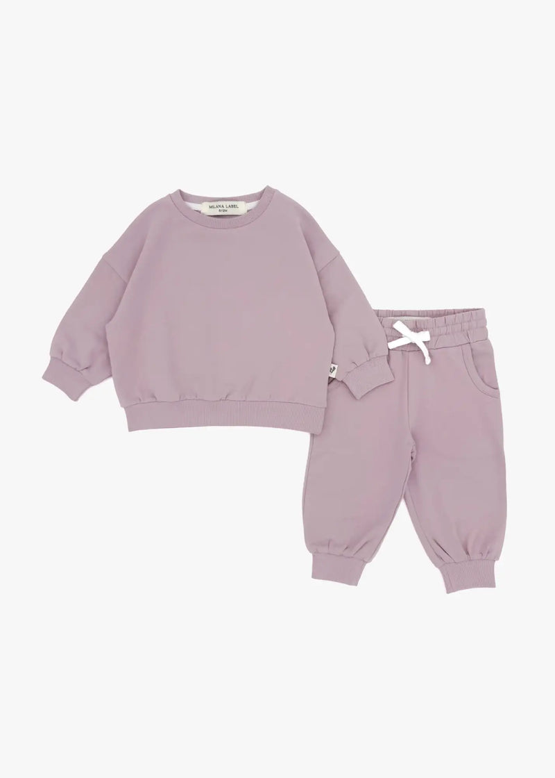 A flat lay product shot of a matching children's organic cotton jogger set in pale orchid, featuring a muted dusty pink oversized sweatshirt and matching jogger pants with a white drawstring bow against a white background.