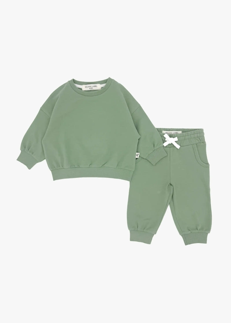 A flat lay product image of a children's two-piece organic cotton loungewear set in eucalyptus green, featuring an oversized crewneck sweatshirt and matching jogger pants with a white drawstring against a plain white background.