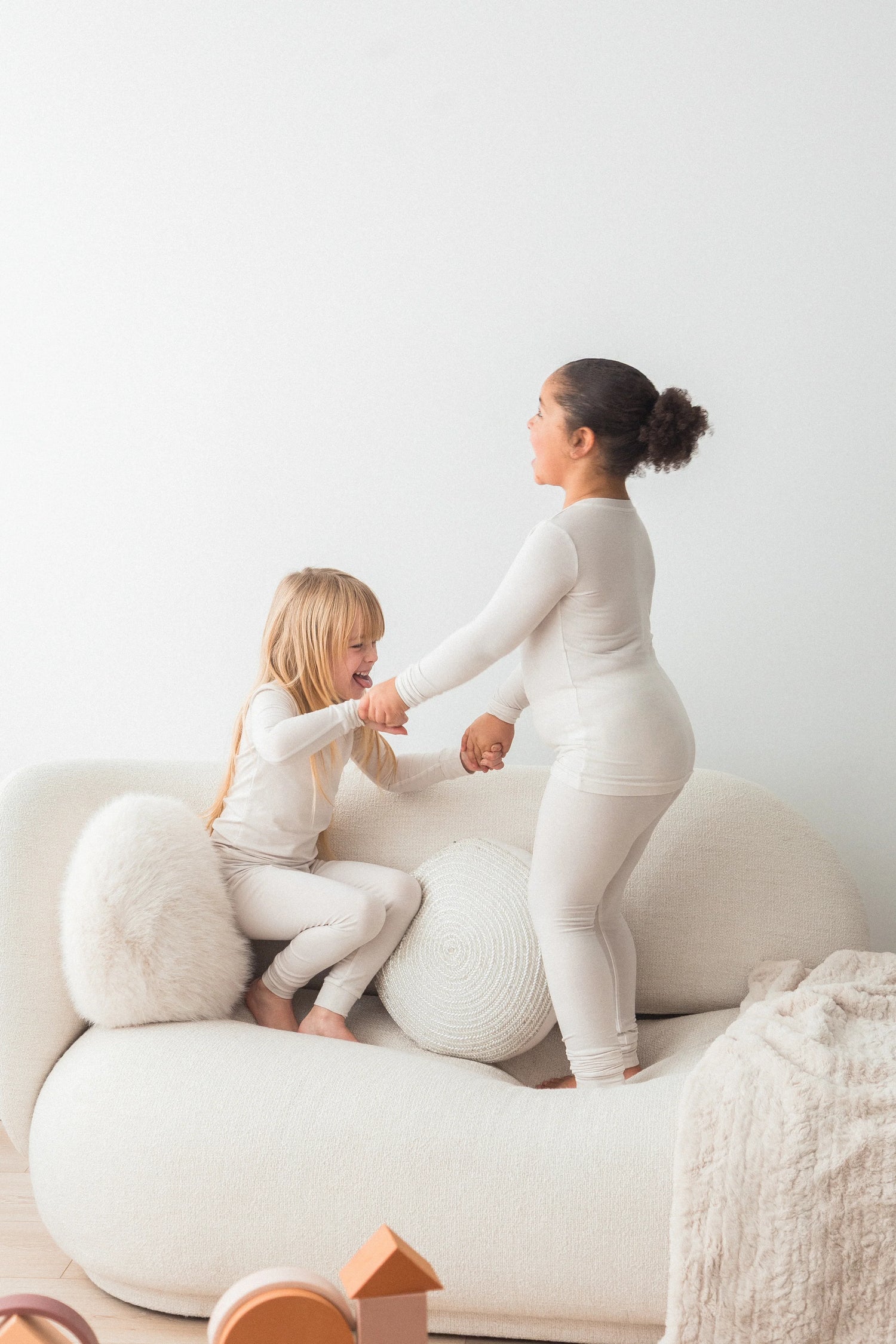 Two girls playing on a a couch in their neutral Milana Label sets.