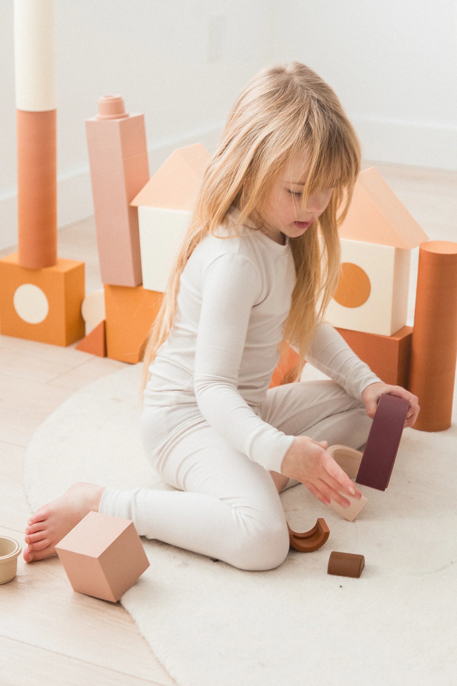 A girl sitting on the floor playing with blocks in her Milana Label neutral pjs.