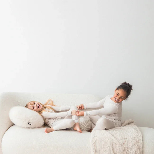 Two girls playing on a a couch in their neutral Milana Label sets.