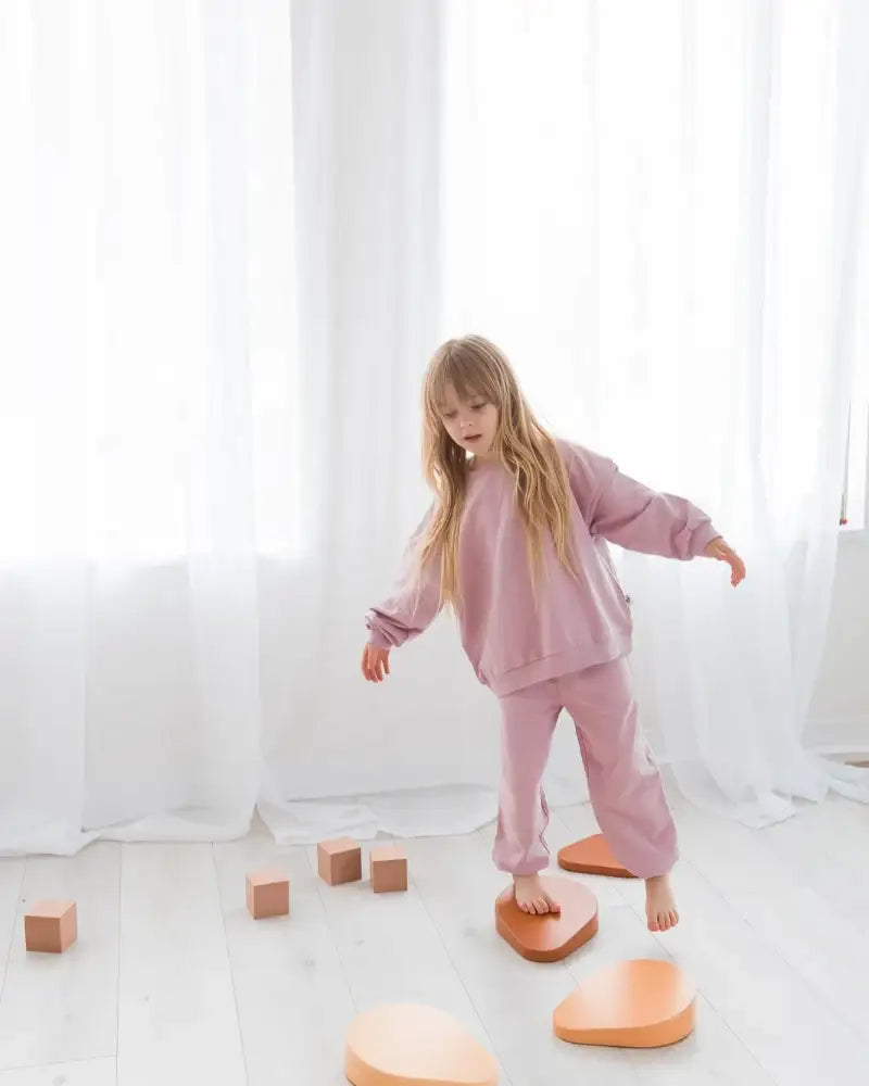 A child wearing a pink sweatshirt and pants set playing on a white floor.