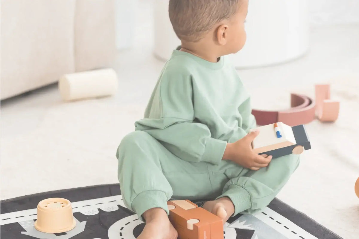 A toddler wearing a green long sleeve top and pants sitting on a play mat.