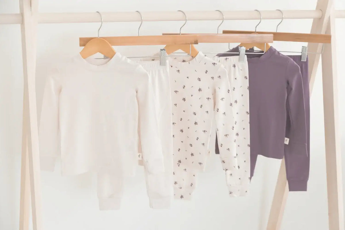 White and purple baby pajamas with a floral print hanging on a wooden rack.