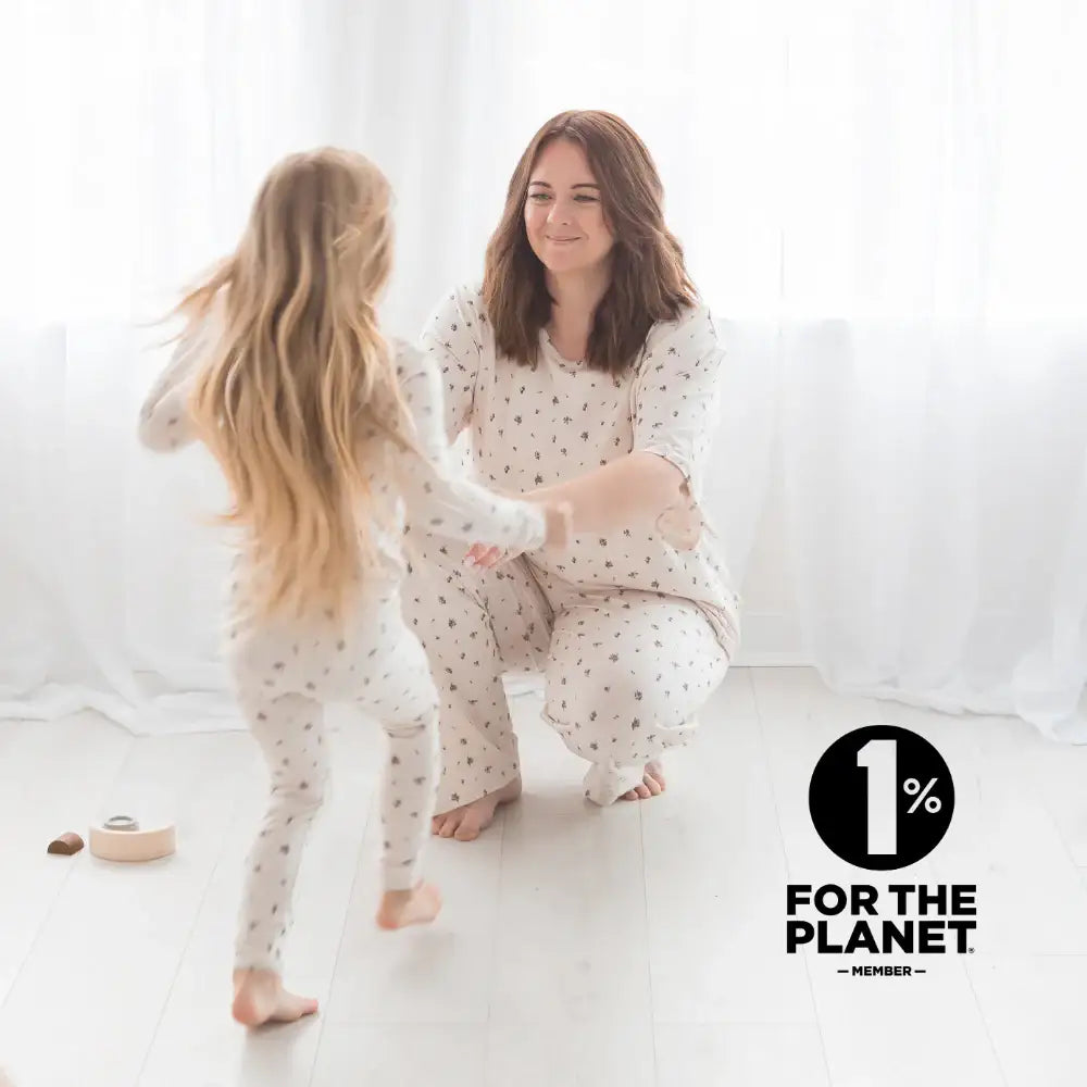 A mother and young girl wearing matching Milana Soft™ Birch Floral pajama sets play together in a bright, sunlit room with the 1% for the Planet logo overlaid.