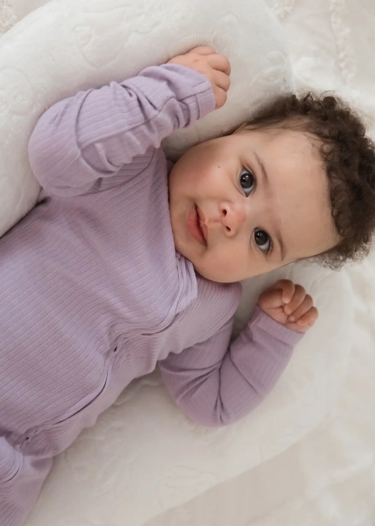 A close-up of a baby looking into the camera wearing a ribbed zippered sleeper.