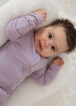 A close-up of a baby looking into the camera wearing a ribbed zippered sleeper.