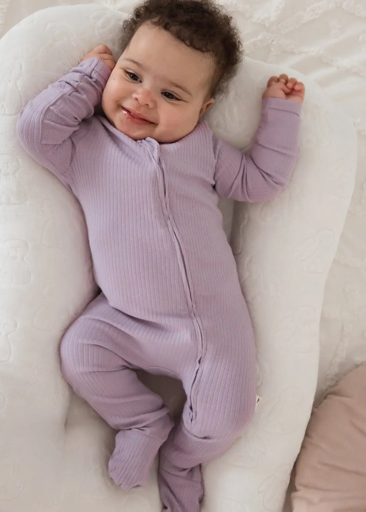 A smiling baby wearing a Lavender Blush organic cotton footie PJ.