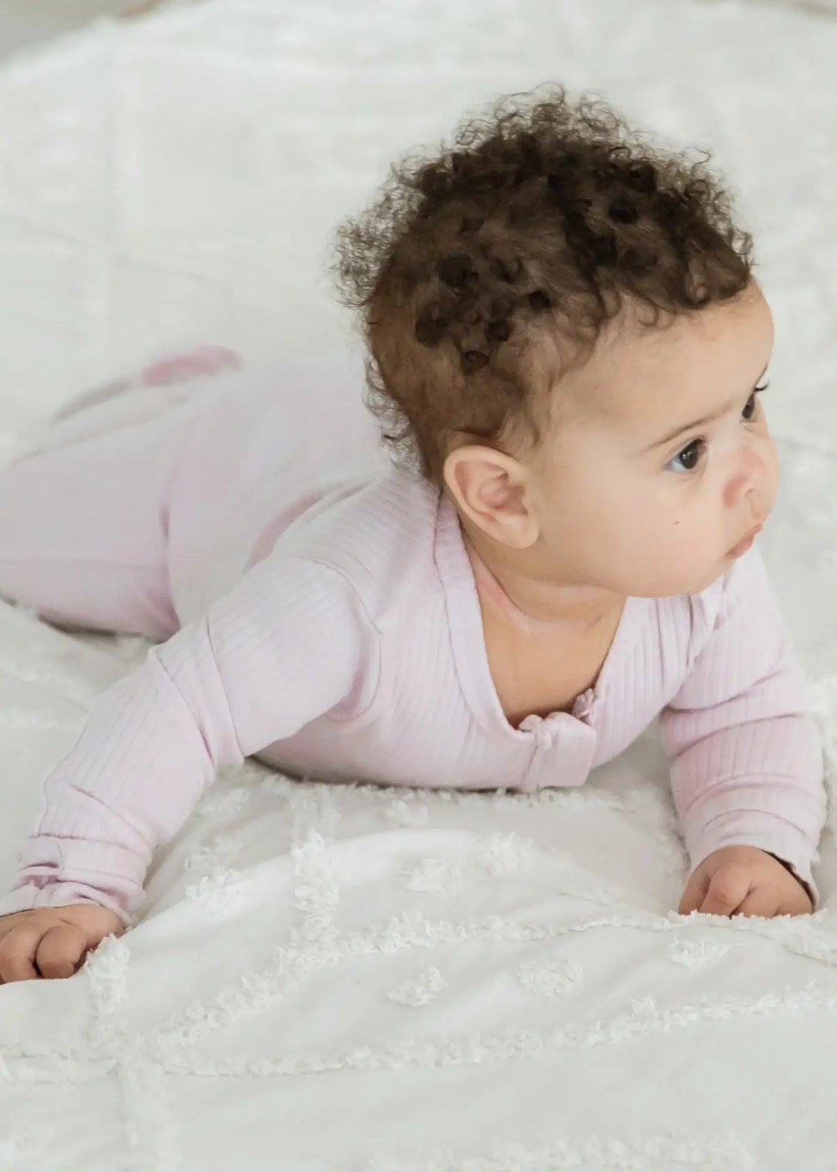 A baby doing tummy time in a ribbed organic cotton footie in the colour Petal pink.