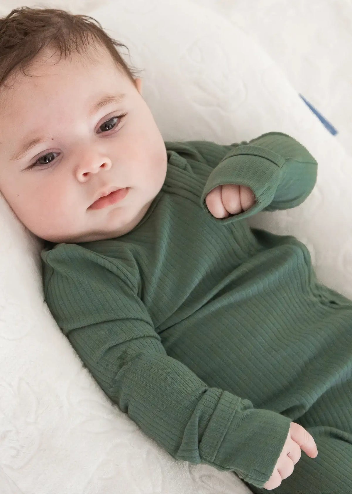 A close-up of a baby wearing a ribbed zippered sleeper from Milana Label.