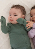 A baby looking at his hands with the fold-over mitts covering them.