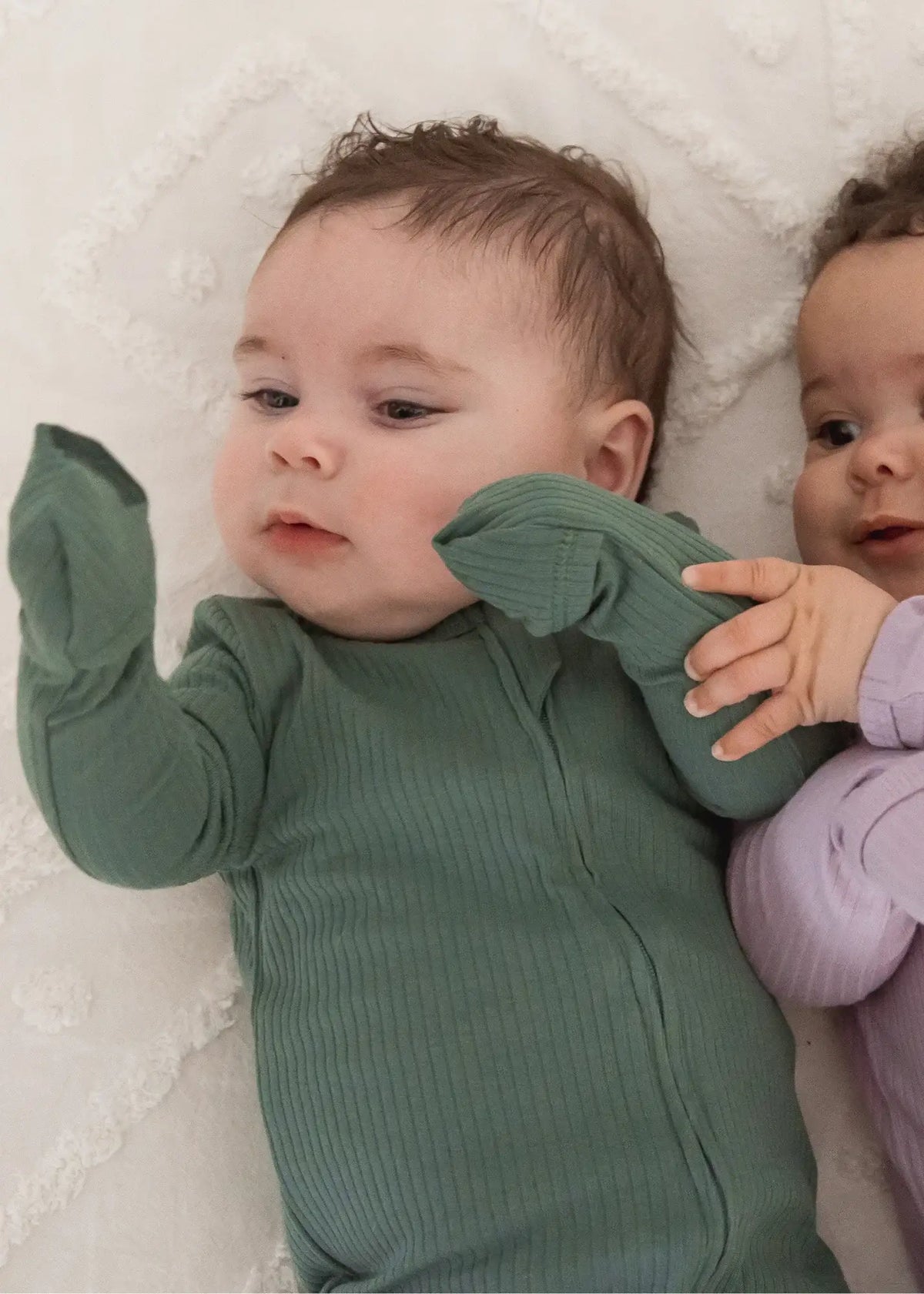 A baby looking at his hands with the fold-over mitts covering them.