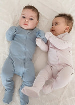 Two babies wearing ribbed zippered sleepers in Soft Slate and Petal.