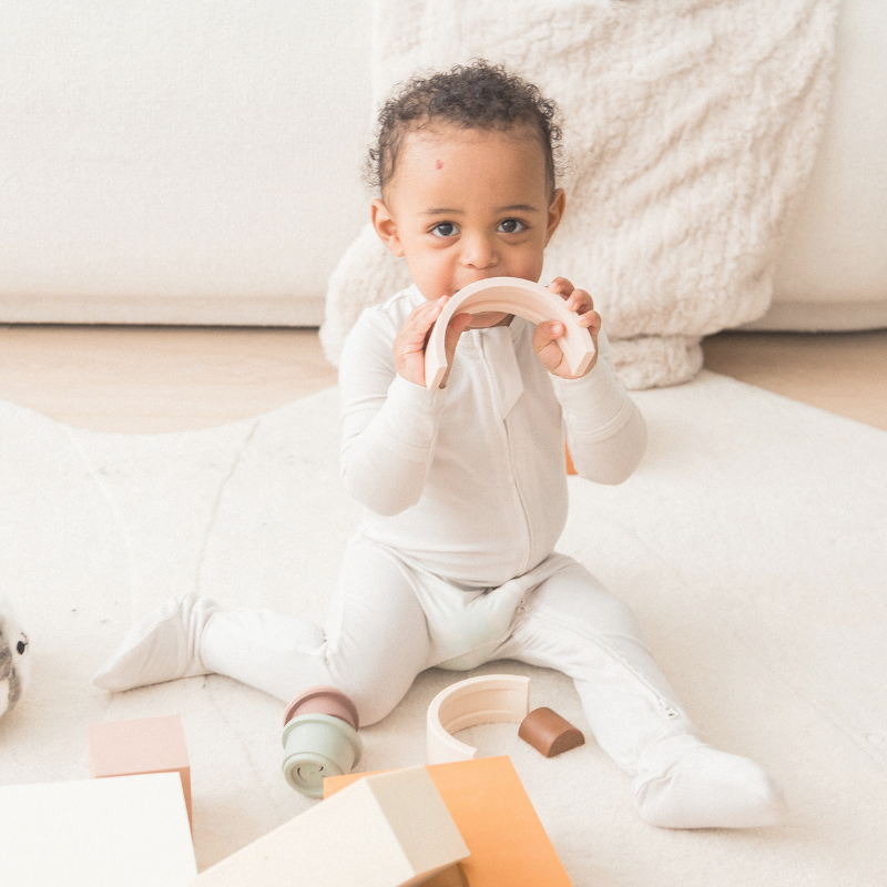 A little boy playing with toys on the floor in his neutral Milana Label sleeper.