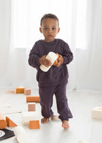 A young boy playing with foam blocks and wearing a matching sweatshirt and pants in the colour Elderberry.