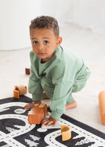 A toddler crouching down to play with wooden cars in his Eucalyptus green jogger set.