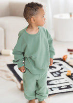 A toddler wearing an oversized organic cotton jogger set in the colour Eucalyptus green.