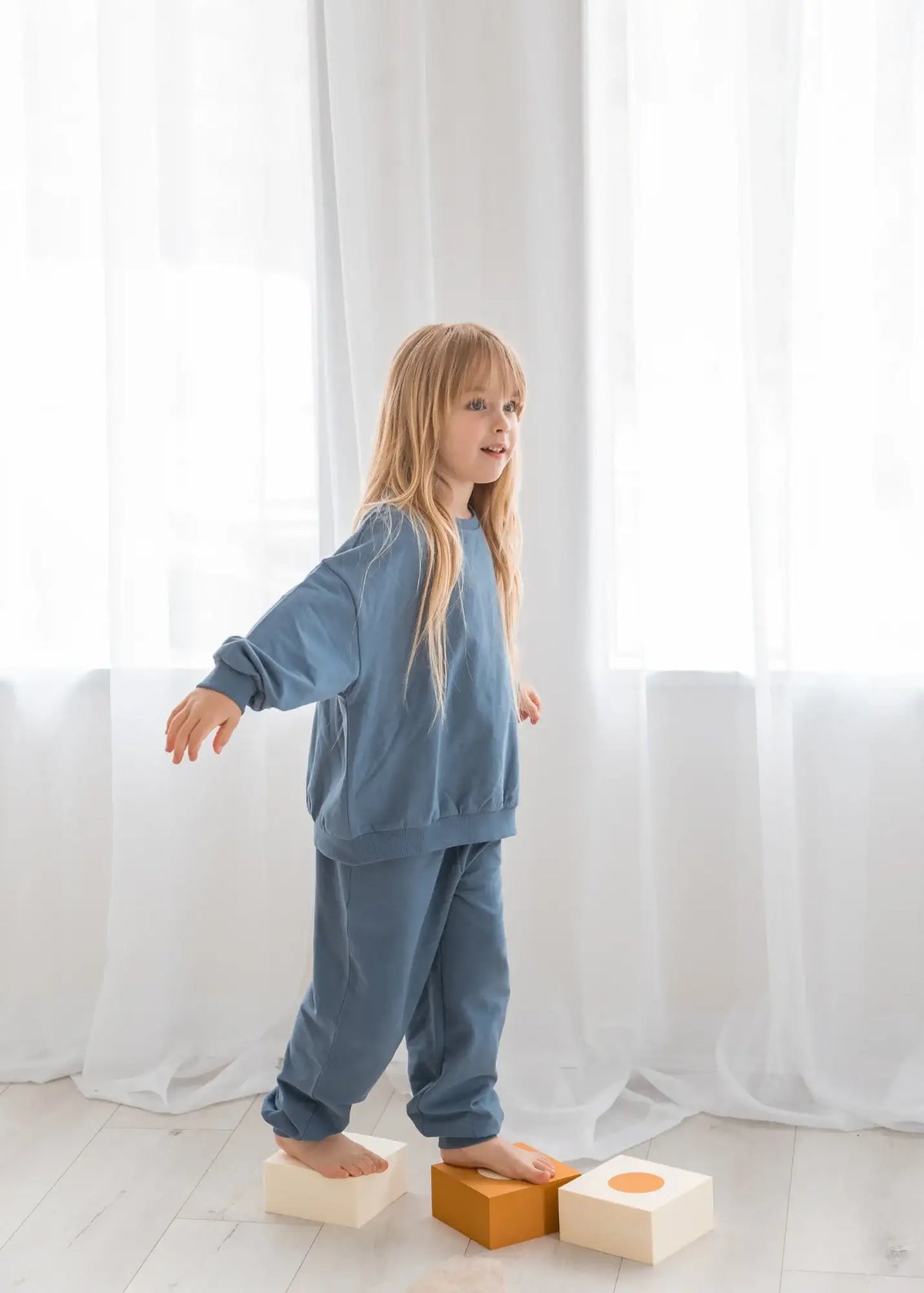A girl balances on foam blocks while wearing a GOTS certified organic Nordic Blue two-piece set.