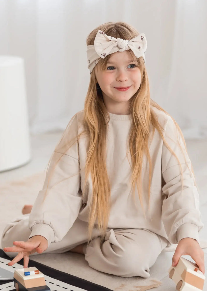 A young girl playing on the floor wearing a neutral Oat coloured jogger set.