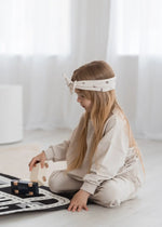 A young girl playing with wooden cars wearing a matching two-piece set in the colour Oat.