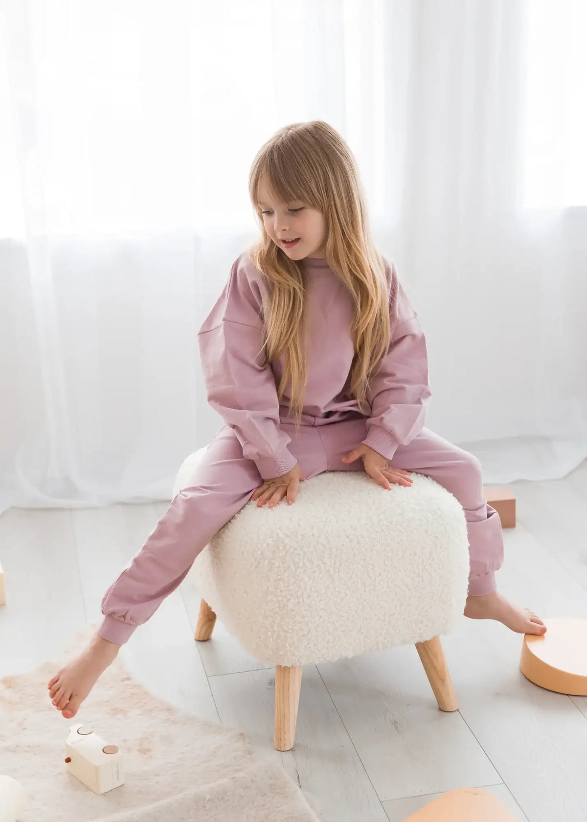 A girl sitting on an ottoman in a Pale Orchid matching two-piece set.