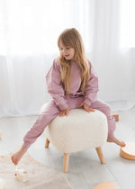 A girl sitting on an ottoman in a Pale Orchid matching two-piece set.