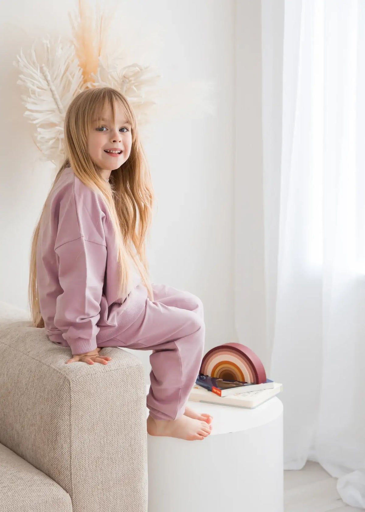 A young girl sitting on a sofa wearing a Pale Orchid organic cotton jogger set.